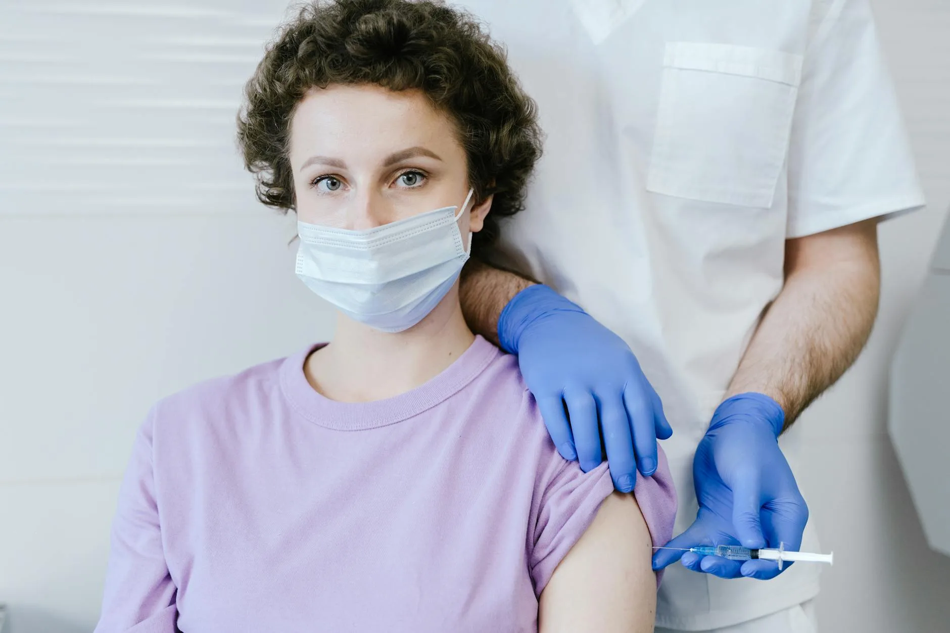 woman in mask sitting and doctor applying syringe with vaccine