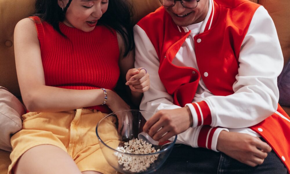 man and woman sitting on the couch while eating popcorn