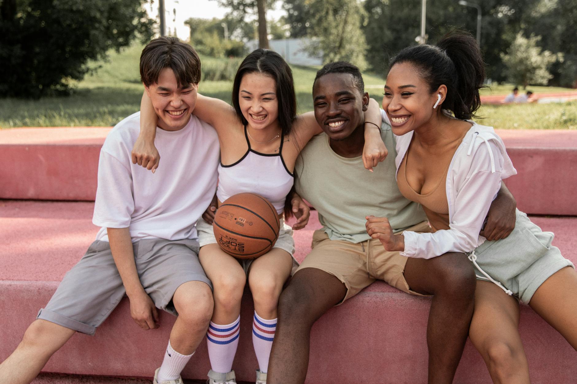 happy multiracial friends embracing on bench after basketball training. Livable communities