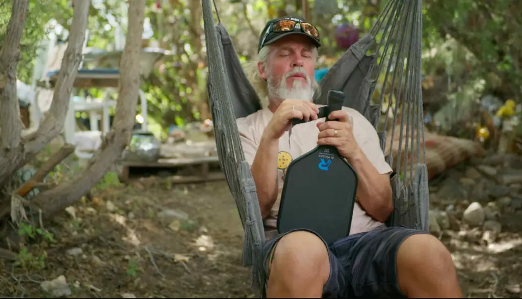 a man sitting in a hammock holding a pickleball paddle. Dreambreaker