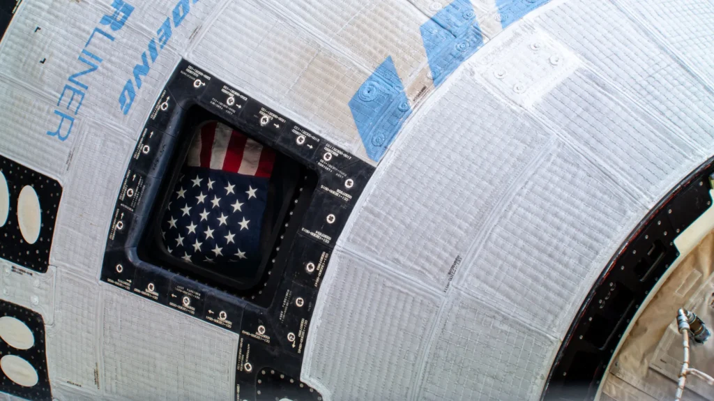 The American flag pictured inside the window of Boeing’s Starliner spacecraft at the International Space Station. Credit: NASA