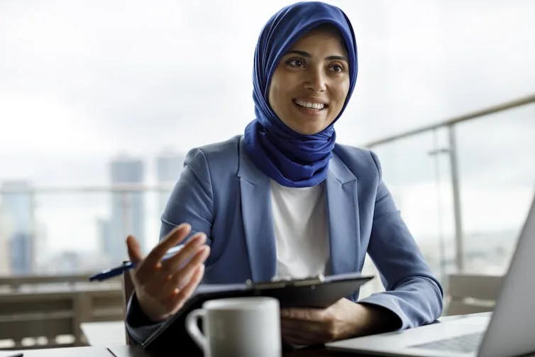 A woman in a blue suit and headscarf gestures with her hand while talking. mortgages