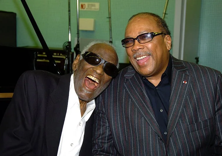 Two Black men wearing black suits laughing.