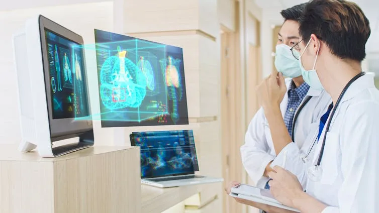 Two male doctors in white coats and face masks stand looking at a complex graphic on two computer screens in front of them.