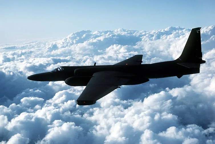 A single-seat jet aircraft with no markings flies high above the clouds