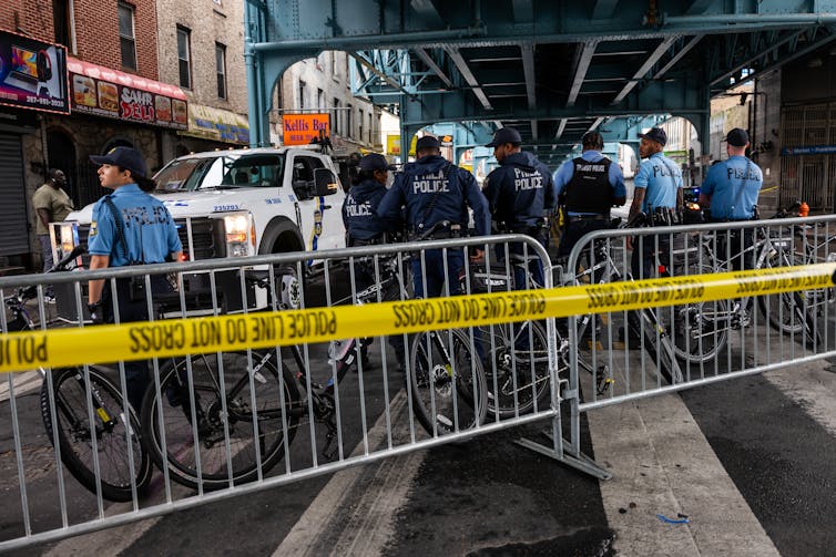 Seven police officers stand behind barrier gate under elevated train track