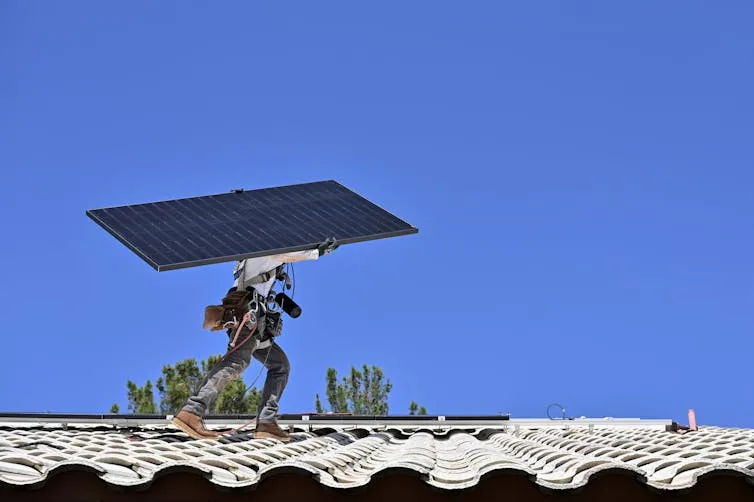 installer on a residential roof carrying a solar panel