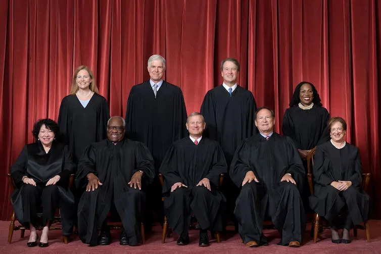 A group of nine people wearing black robes pose for a portrait.