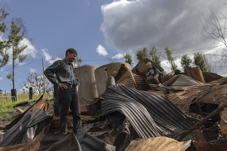 A man and a child stand amid wreckage that's been burned.