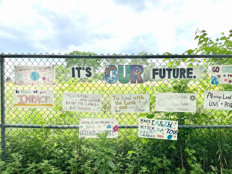 Hand-drawn signs displayed on a fence against a green field, with messages about climate change around a sign that reads 'It's our future'