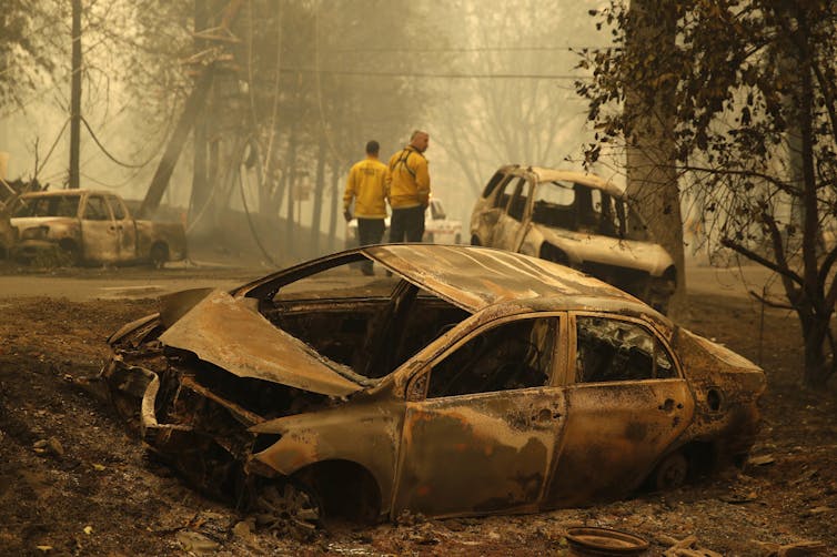 Firefighters walk near three burned out vehicles on the side of roads.