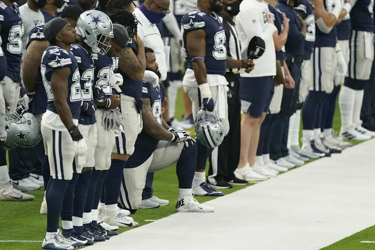 An NFL player kneels on the sidelines of a football field.