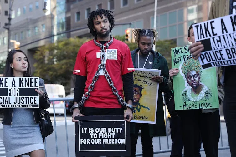 A Black activist wearing chains, surrounded by other protesters, calls for an end to police brutality.