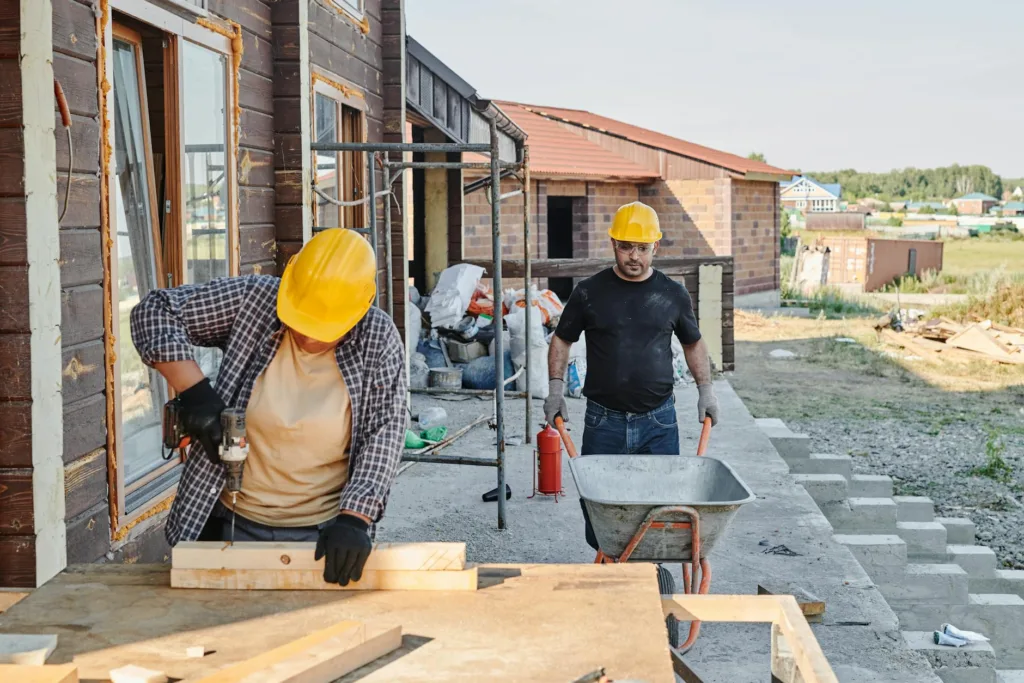 man in black shirt wearing yellow hard hat pushing barrow. Housing